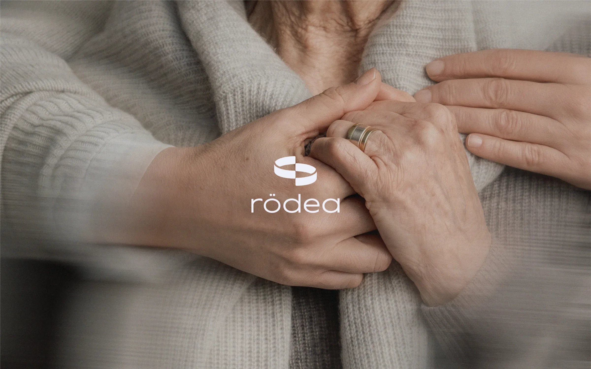 A younger hand and an older hand held together warmly, with the rödea logo